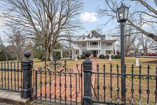 neoclassical home featuring a balcony, a fenced front yard, a chimney, a gate, and a front yard