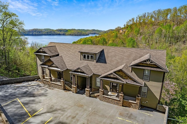 view of front of house with a patio area, stone siding, a water view, and roof with shingles