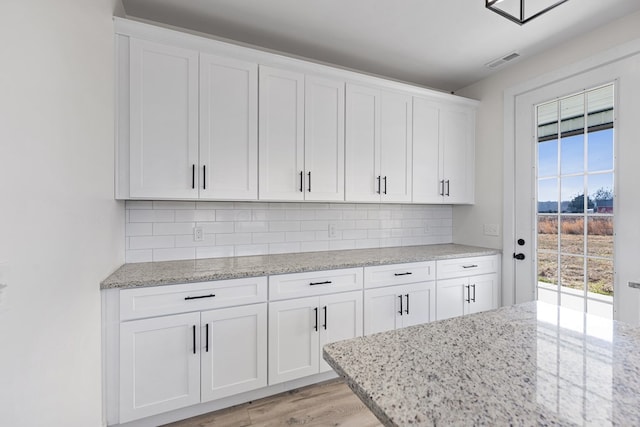 kitchen featuring visible vents, decorative backsplash, light wood-style flooring, light stone countertops, and white cabinetry