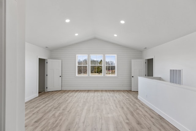 spare room with lofted ceiling, light wood finished floors, visible vents, and baseboards