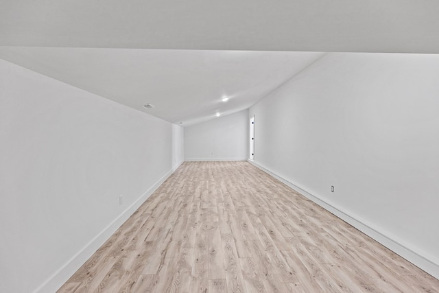 unfurnished room with light wood-style floors, visible vents, vaulted ceiling, and baseboards