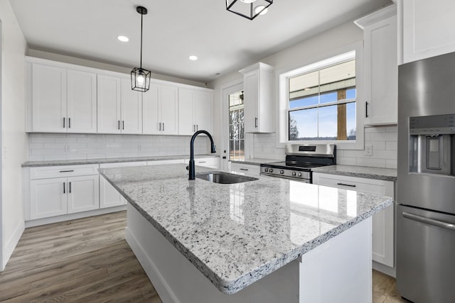 kitchen featuring appliances with stainless steel finishes, white cabinets, a center island with sink, and a sink