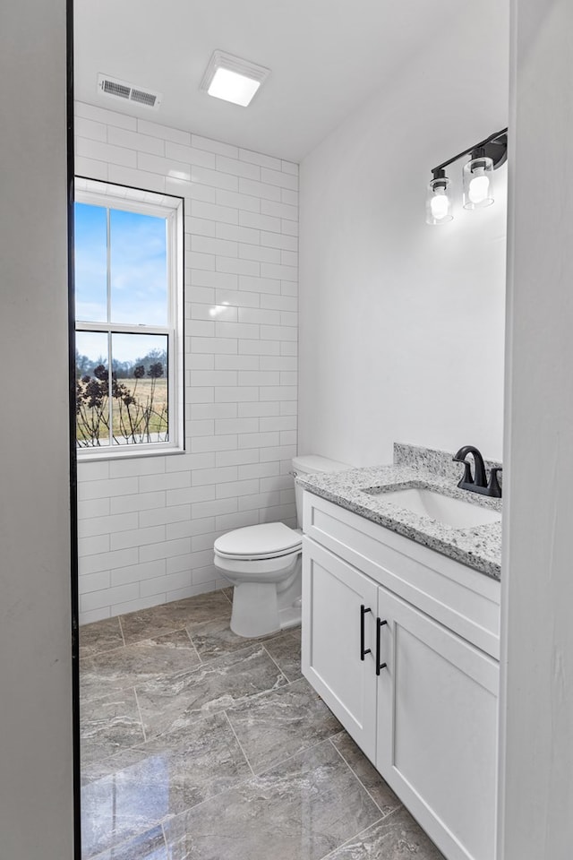 full bath featuring toilet, visible vents, tile walls, and vanity