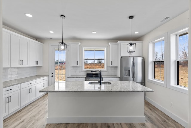 kitchen featuring white cabinets, a kitchen island with sink, stainless steel appliances, pendant lighting, and a sink