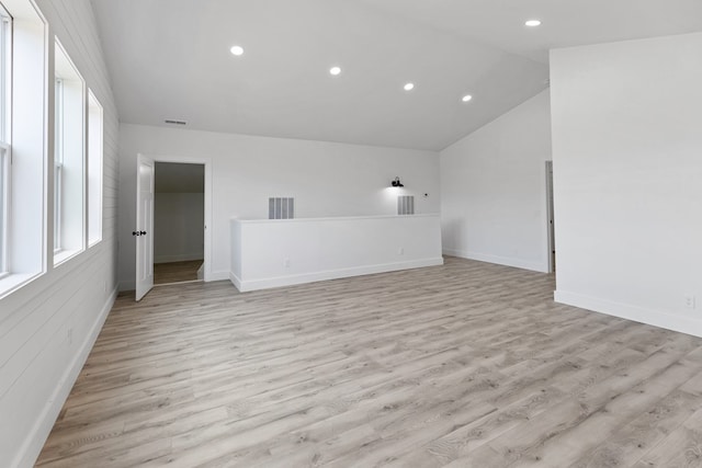 empty room featuring lofted ceiling, light wood-style floors, baseboards, and visible vents