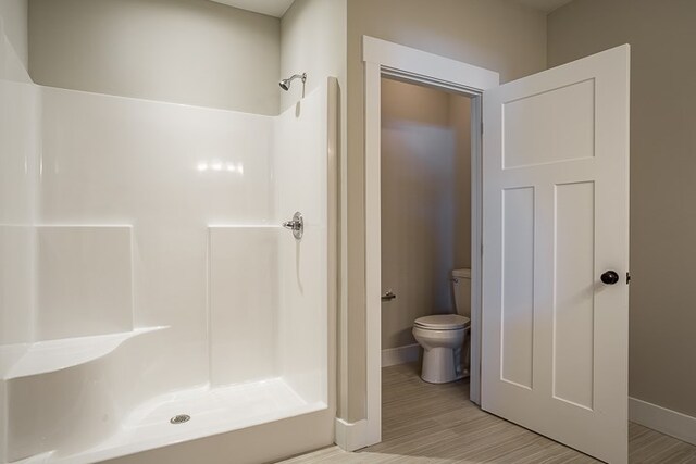 bathroom with toilet, a stall shower, baseboards, and wood finished floors