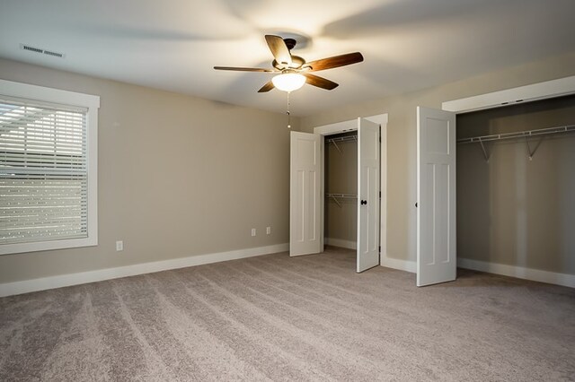 unfurnished bedroom with multiple closets, visible vents, light carpet, and baseboards