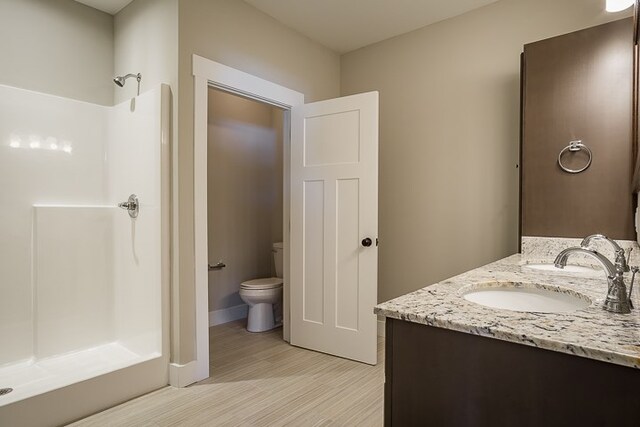 bathroom with toilet, wood finished floors, a sink, a shower stall, and double vanity