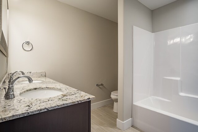 bathroom with toilet, wood finished floors, a sink, baseboards, and double vanity