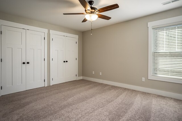 unfurnished bedroom with ceiling fan, carpet floors, visible vents, baseboards, and multiple closets