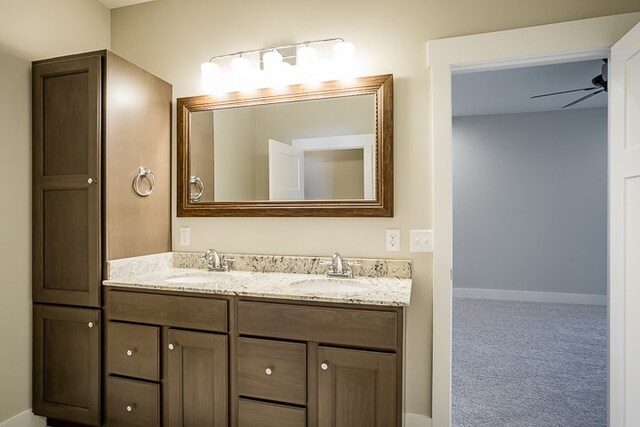 full bath featuring ceiling fan, double vanity, a sink, and baseboards