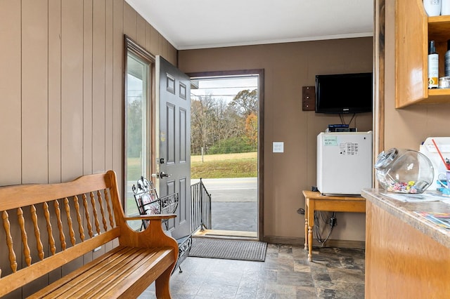 entryway with stone finish flooring, ornamental molding, wood walls, and baseboards