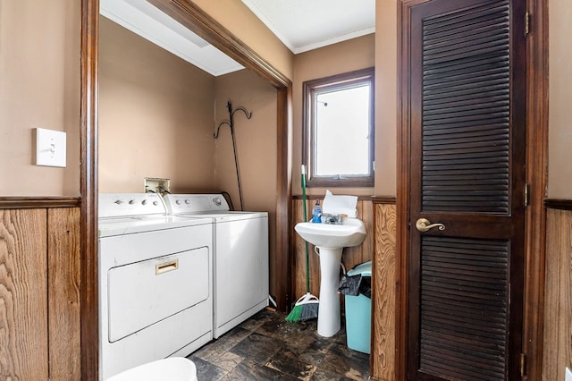 clothes washing area with stone finish flooring, wainscoting, crown molding, and washing machine and clothes dryer