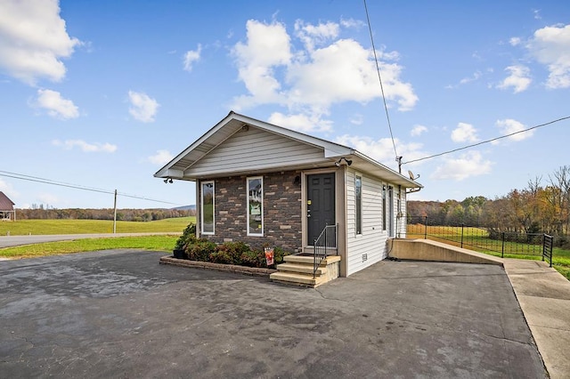 shotgun-style home with stone siding, fence, and aphalt driveway