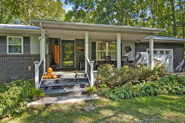 doorway to property with an attached garage, a porch, and brick siding