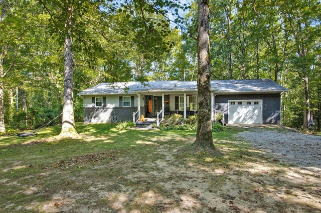 single story home with a garage, a front lawn, a porch, and gravel driveway