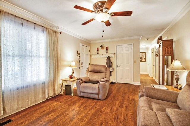 living room featuring dark wood-style flooring, a ceiling fan, baseboards, visible vents, and crown molding