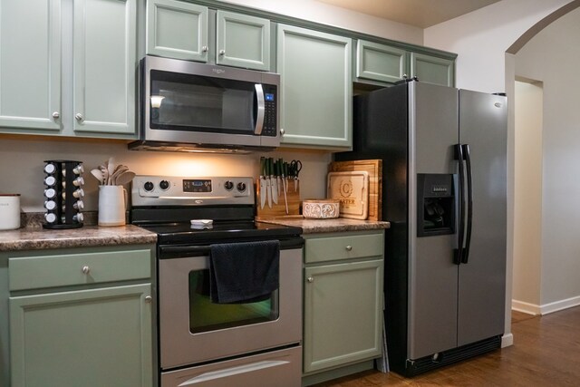 kitchen featuring dark wood-style floors, arched walkways, stainless steel appliances, dark countertops, and green cabinetry