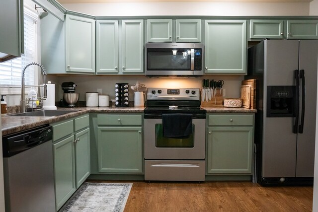 kitchen with stainless steel appliances, dark countertops, light wood-style floors, a sink, and green cabinetry