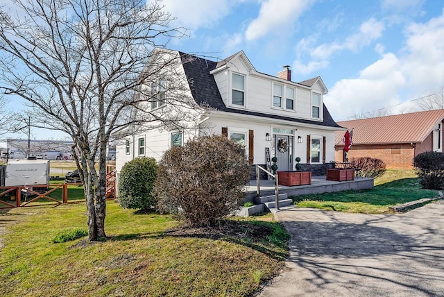 view of front facade with a shingled roof, fence, a gambrel roof, a chimney, and a front yard