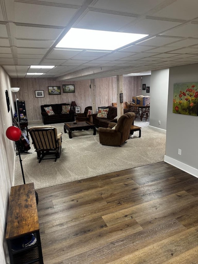 living room with a drop ceiling, wooden walls, baseboards, and wood finished floors