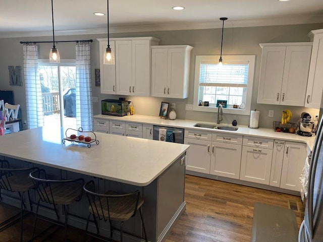 kitchen featuring dishwashing machine, a kitchen breakfast bar, wood finished floors, crown molding, and a sink