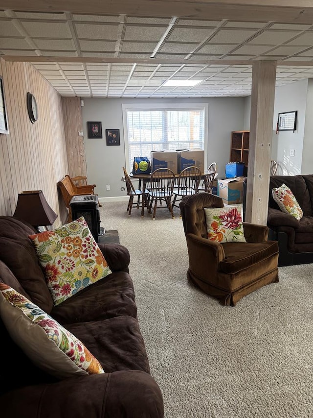 carpeted living room featuring a paneled ceiling, wood walls, and baseboards