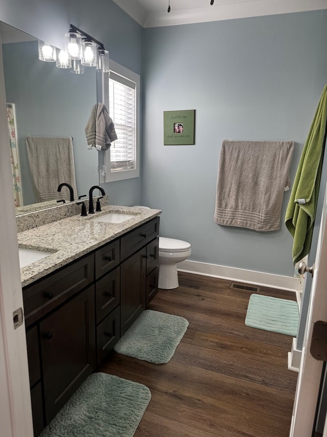 full bath with toilet, wood finished floors, a sink, baseboards, and double vanity