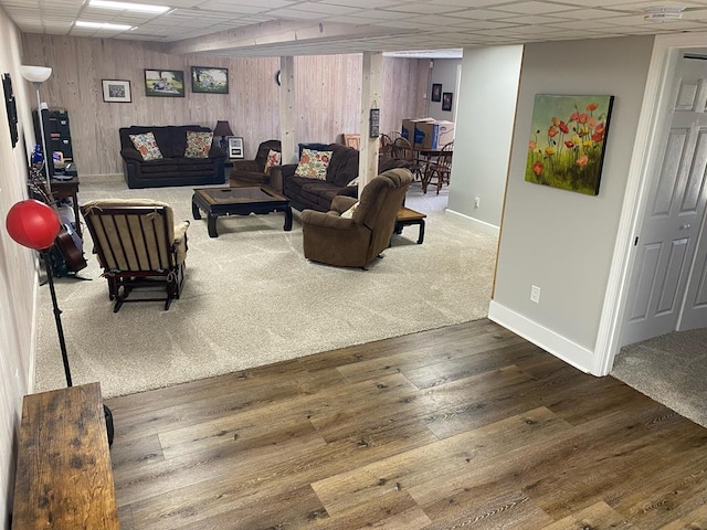 living room with a paneled ceiling, wood walls, baseboards, and hardwood / wood-style flooring