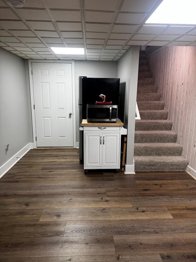 finished basement featuring stairs, a drop ceiling, dark wood finished floors, and baseboards