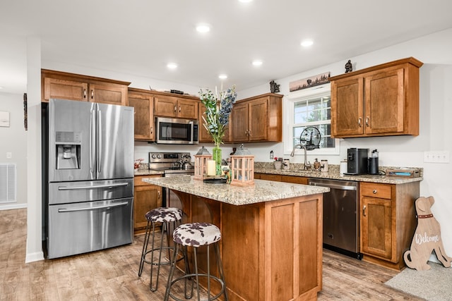 kitchen with light stone countertops, a center island, a kitchen breakfast bar, appliances with stainless steel finishes, and brown cabinets