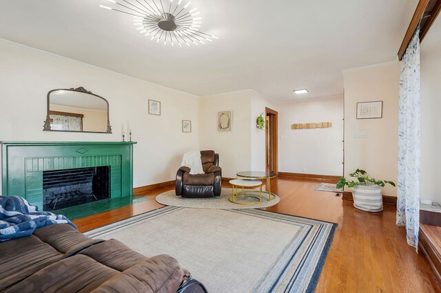 living area featuring baseboards, a brick fireplace, wood finished floors, and crown molding