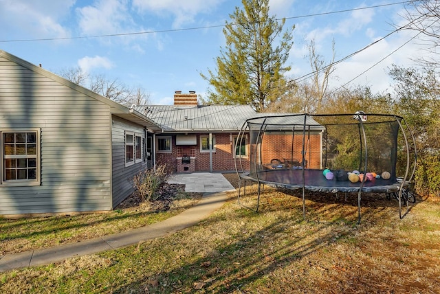 rear view of property with a lawn, a patio, a chimney, a trampoline, and brick siding