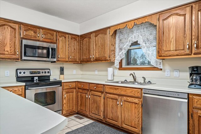 kitchen featuring light countertops, appliances with stainless steel finishes, brown cabinetry, and a sink