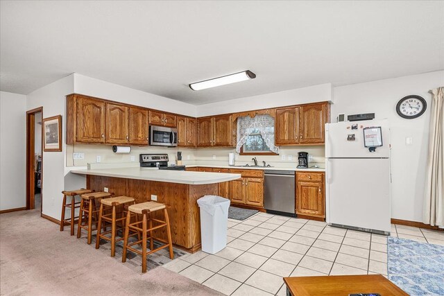 kitchen featuring stainless steel appliances, light countertops, brown cabinetry, a peninsula, and a kitchen bar