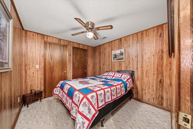 bedroom with a ceiling fan, light colored carpet, visible vents, and wood walls