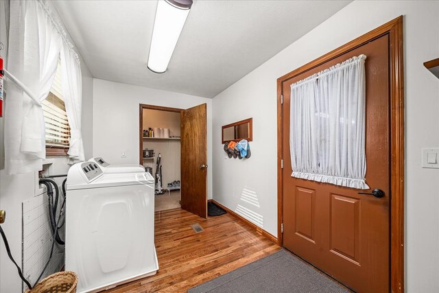 clothes washing area featuring laundry area, washing machine and clothes dryer, light wood-style flooring, and baseboards