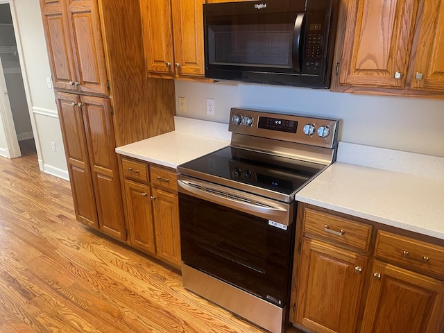 kitchen featuring black microwave, baseboards, stainless steel electric range, light wood finished floors, and brown cabinetry