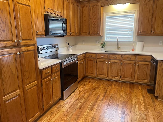 kitchen featuring light wood-style flooring, a sink, light countertops, brown cabinets, and black appliances