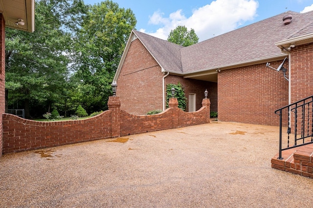 view of property exterior featuring a shingled roof, a patio area, and brick siding