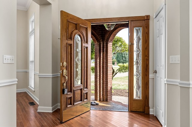 foyer with ornamental molding, wood finished floors, visible vents, and baseboards