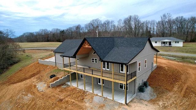 view of front of home featuring a deck, central AC unit, a patio area, and roof with shingles