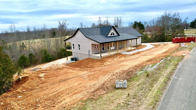 modern farmhouse with a shingled roof, covered porch, central AC, and dirt driveway