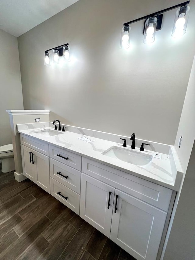 bathroom featuring double vanity, wood finish floors, a sink, and toilet