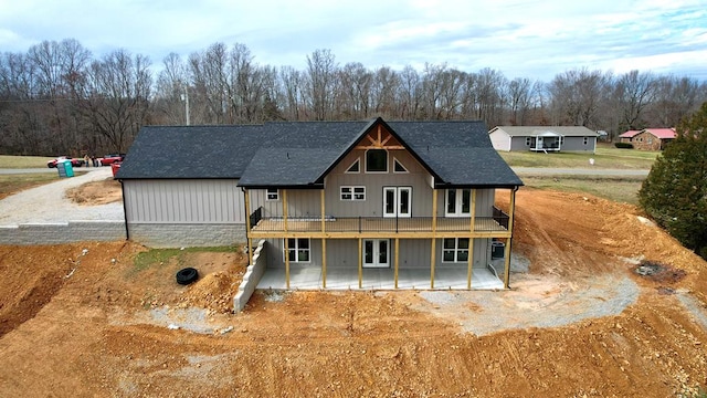 rear view of house with a shingled roof, a patio, a deck, and dirt driveway