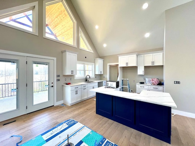 kitchen featuring a sink, white cabinetry, baseboards, light wood-type flooring, and an island with sink