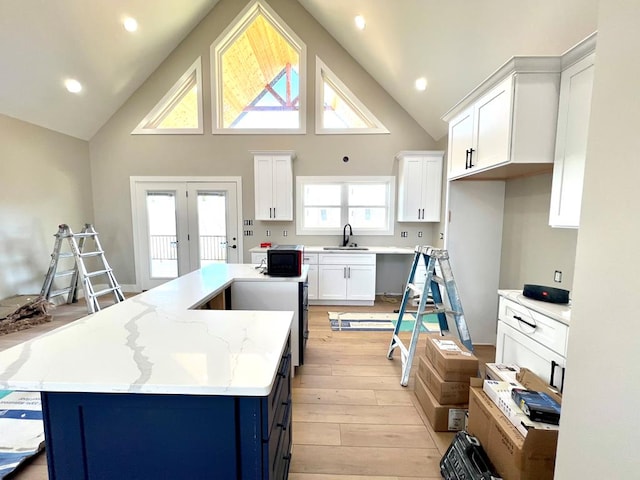 kitchen featuring light stone counters, a kitchen island, a sink, and white cabinetry