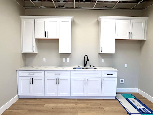 kitchen with light wood-style floors, a sink, white cabinetry, and baseboards