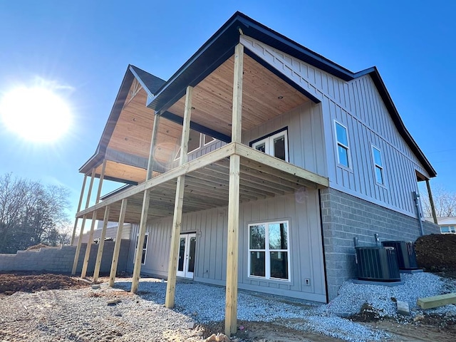 back of house with a carport, a balcony, cooling unit, and board and batten siding