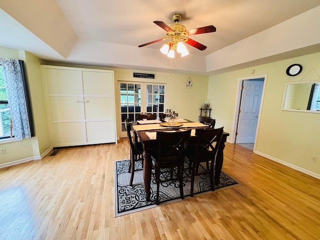 dining area featuring a raised ceiling, ceiling fan, light wood-style flooring, and baseboards